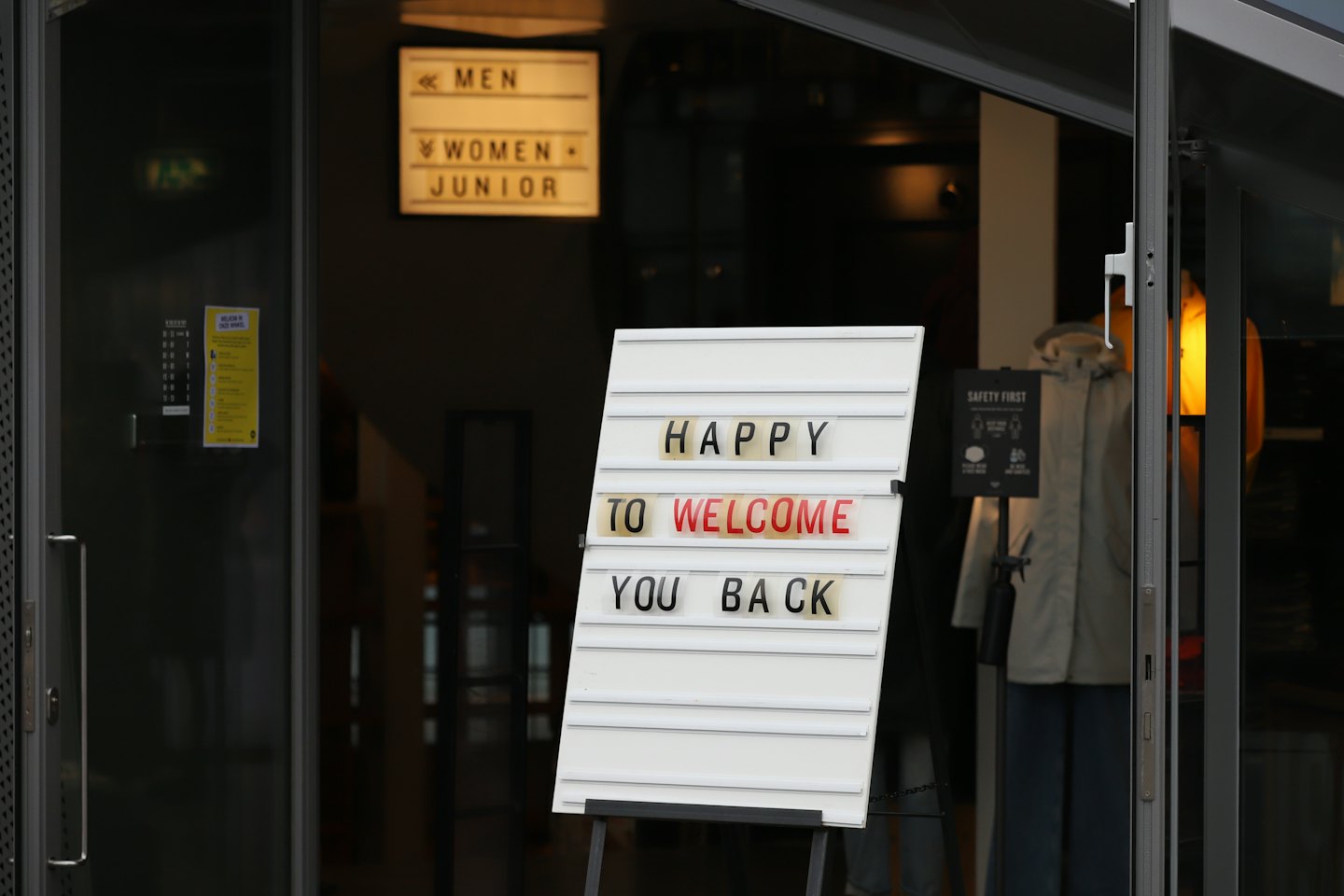 Retail store entrance with 'HAPPY TO WELCOME YOU BACK' sign.