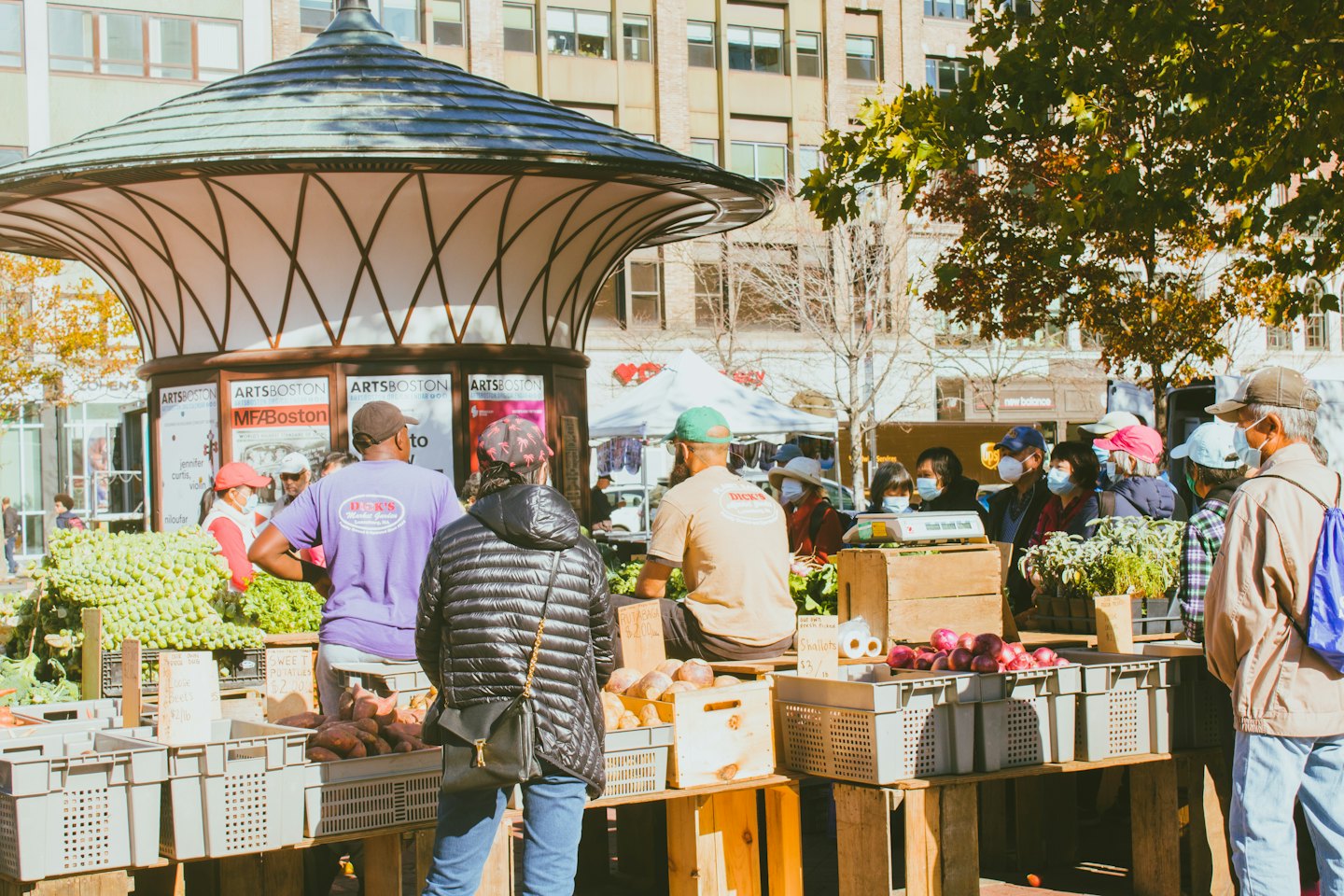 Vendors and shoppers interact at a busy outdoor produce market.